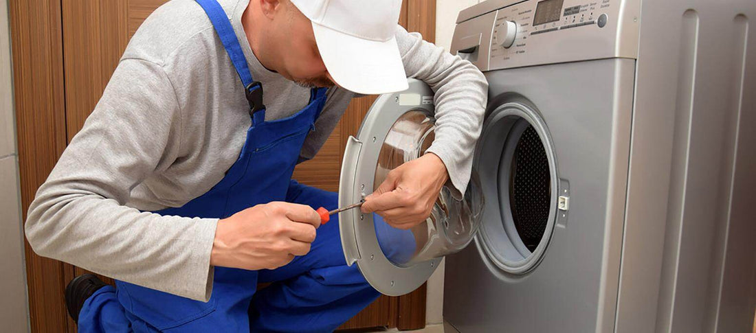 Tecnico in tuta blu che esegue assistenza tecnica asciugatrici riparando un modello frontale moderno