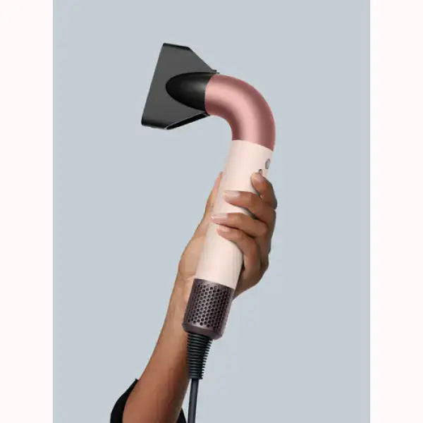 Asciugacapelli Dyson rosa e bianco tenuto in mano con bocchetta concentratrice nera