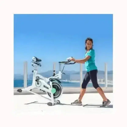 Donna che regola Cecotec Spin Bike bianca su terrazza al mare con sedile e manubrio regolabili per allenamento